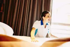 Smiling female making a bed in a hotel room.
